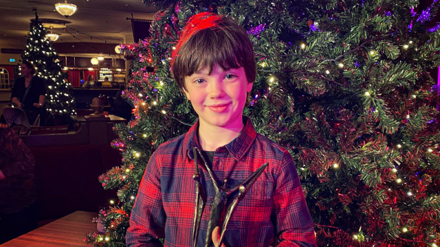 Sten poseert met een grote glimlach met zijn award voor een grote kerstboom
